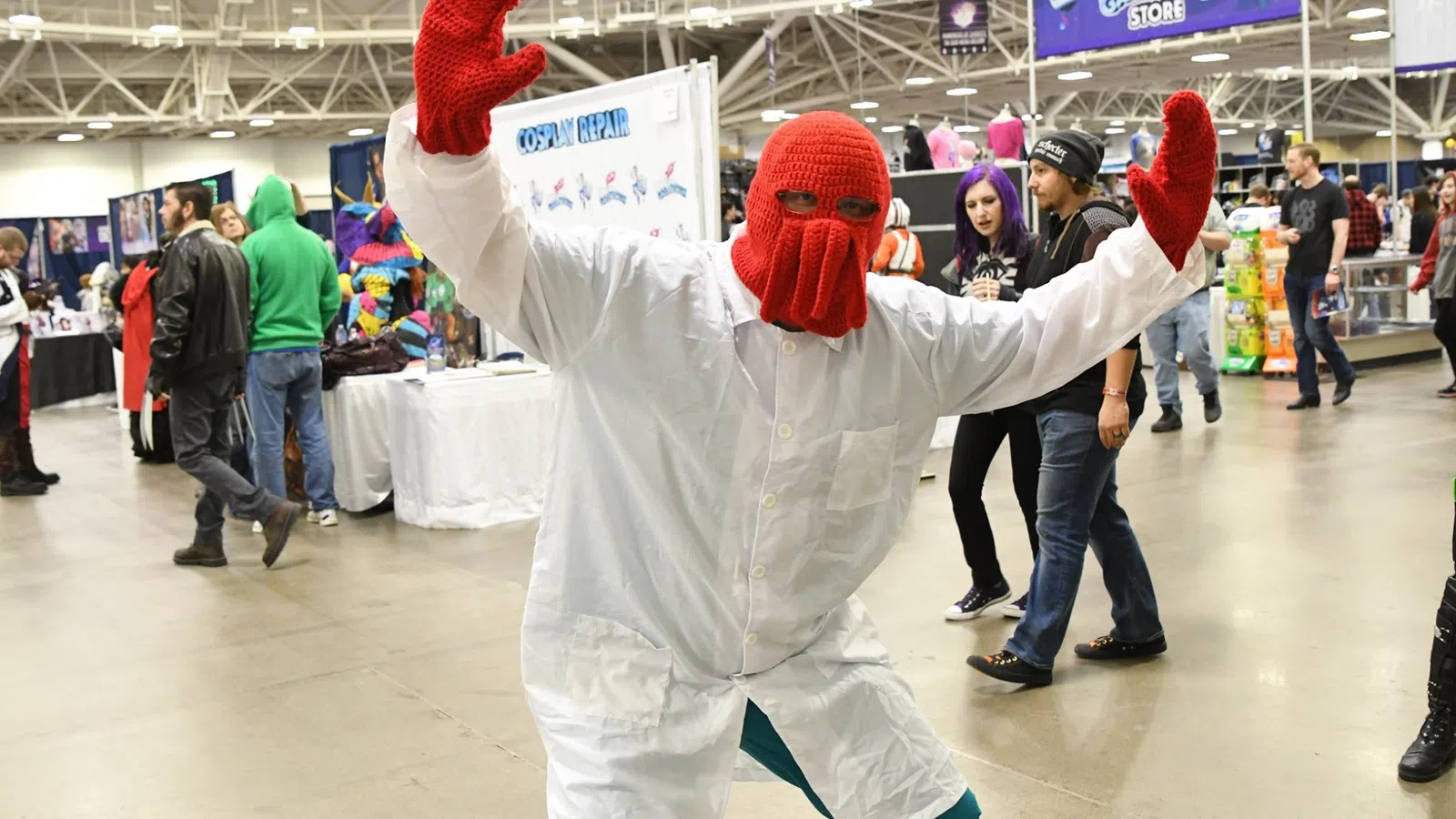 Person dressed as Dr. Zoidberg in a white lab coat and red knitted mask at a convention.