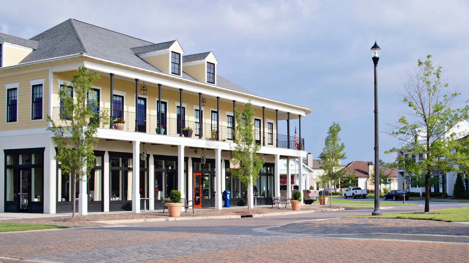 Two-story yellow building with balconies and columns on a cobblestone street in a quiet neighborhood