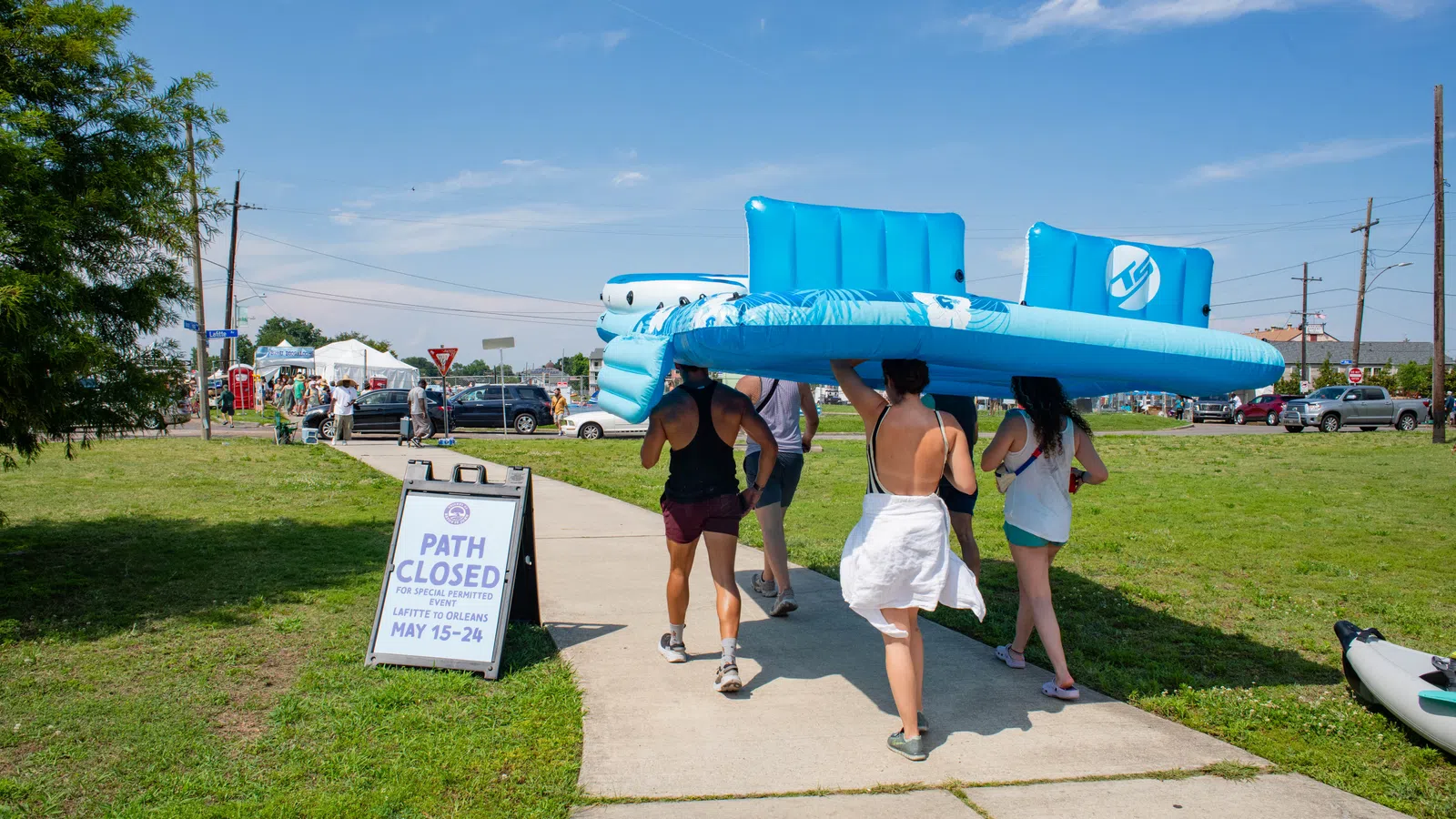 Group carrying large blue float at summer event with a closed path sign in the background.