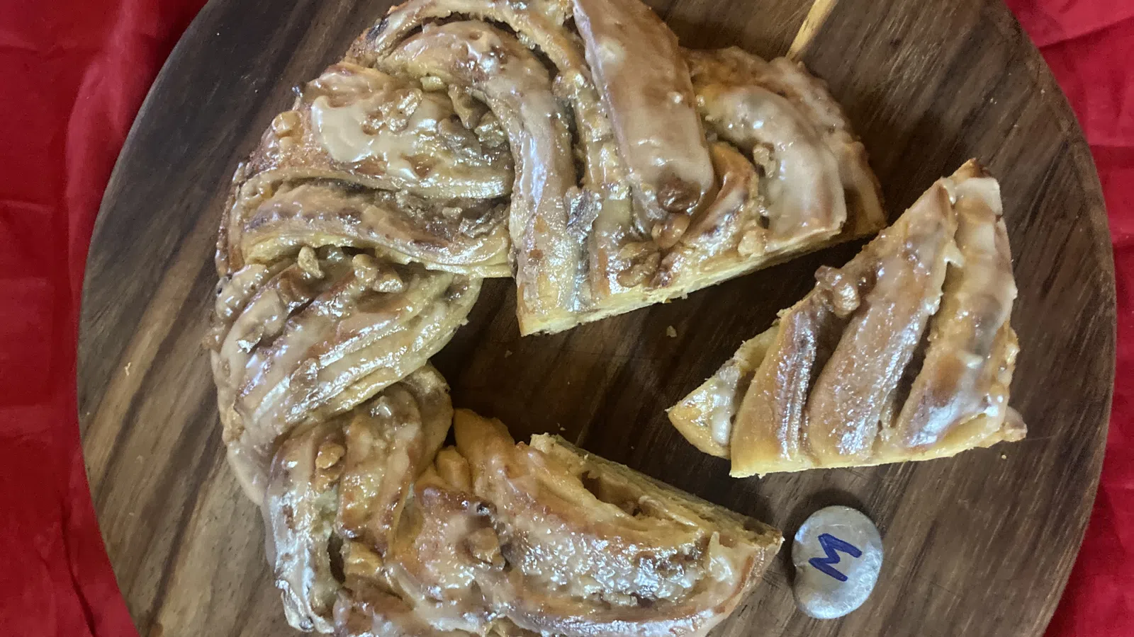 Glazed cinnamon roll wreath with nuts sliced on a wooden board over red cloth background