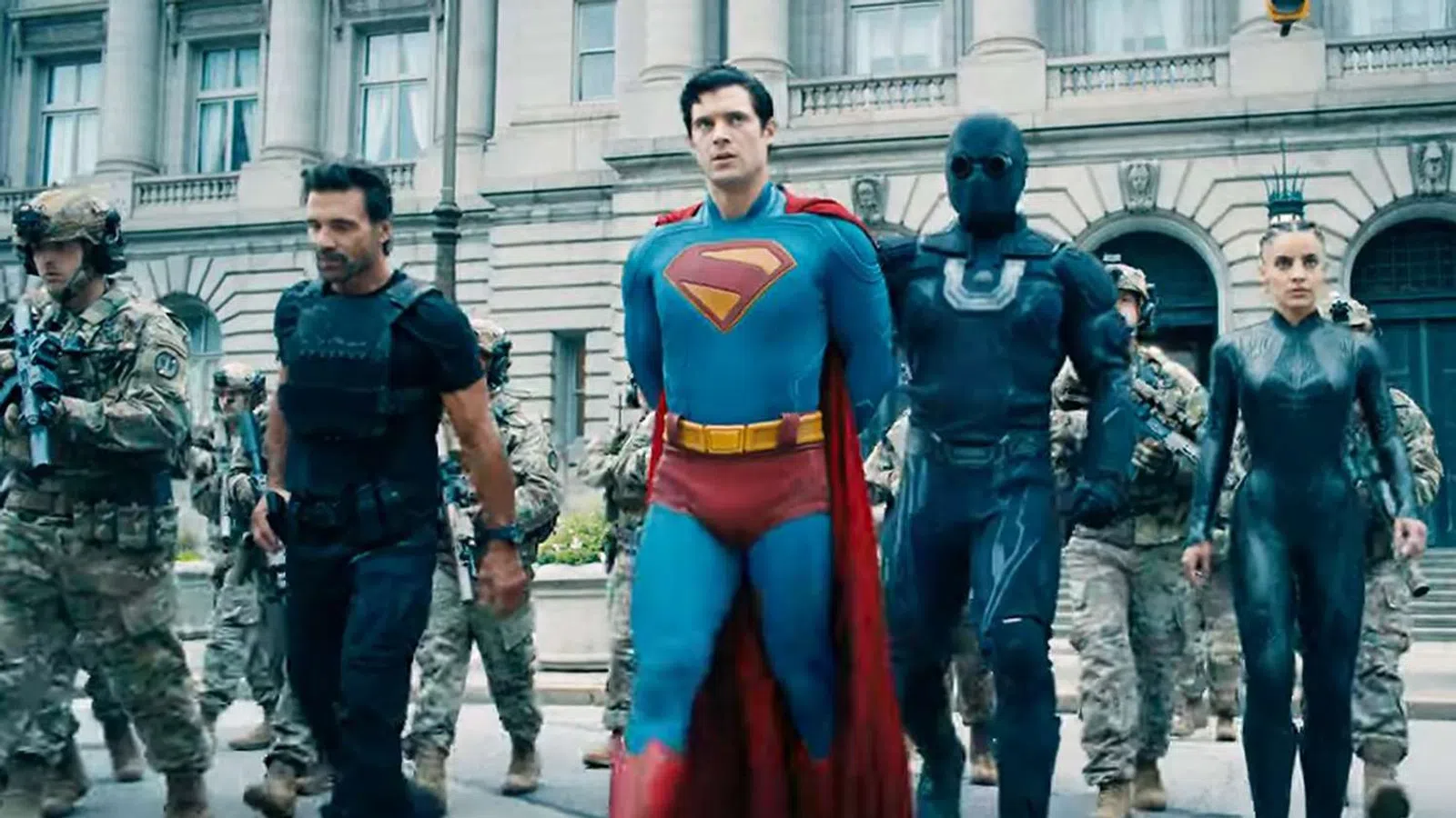 Superheroes including Superman and armed soldiers walking together in front of a classical government building.