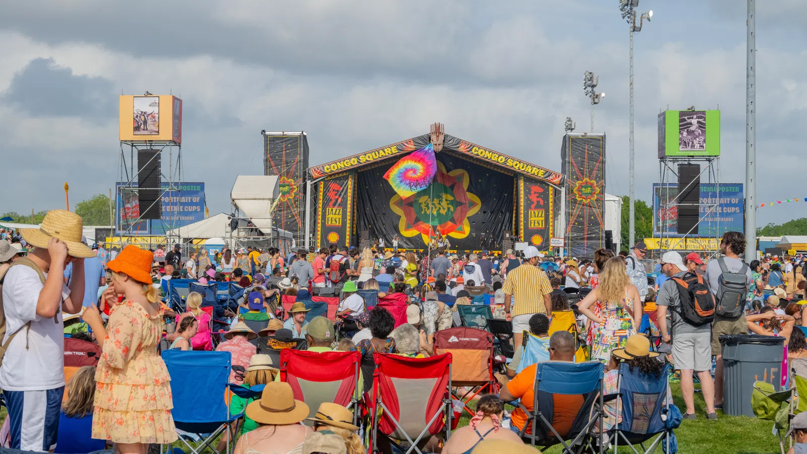 Crowd enjoying a music festival under sunny skies, featuring vibrant stage decorations and tents.