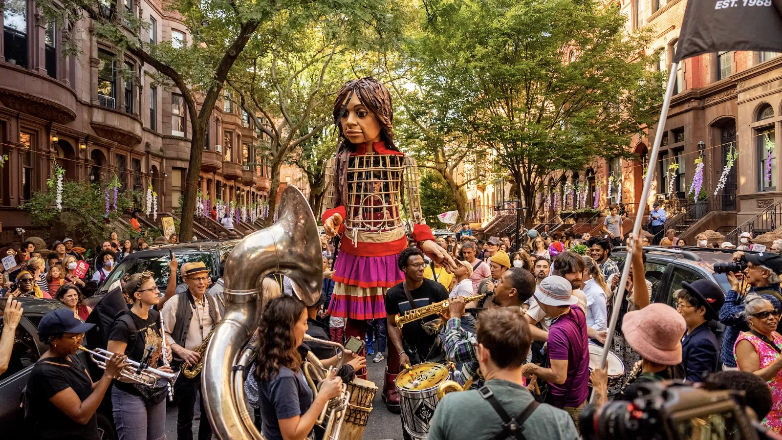 a person in a dress playing a musical instrument in front of a crowd with La Rambla, Barcelona in the background