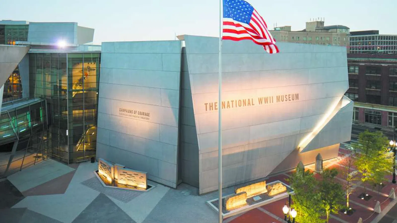 Exterior view of The National WWII Museum with an American flag waving in front during dusk.
