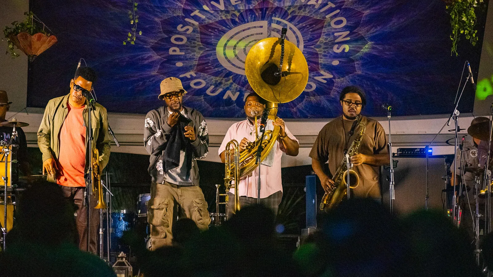 Jazz band performing live on stage with brass instruments under Positive Vibrations Foundation banner.