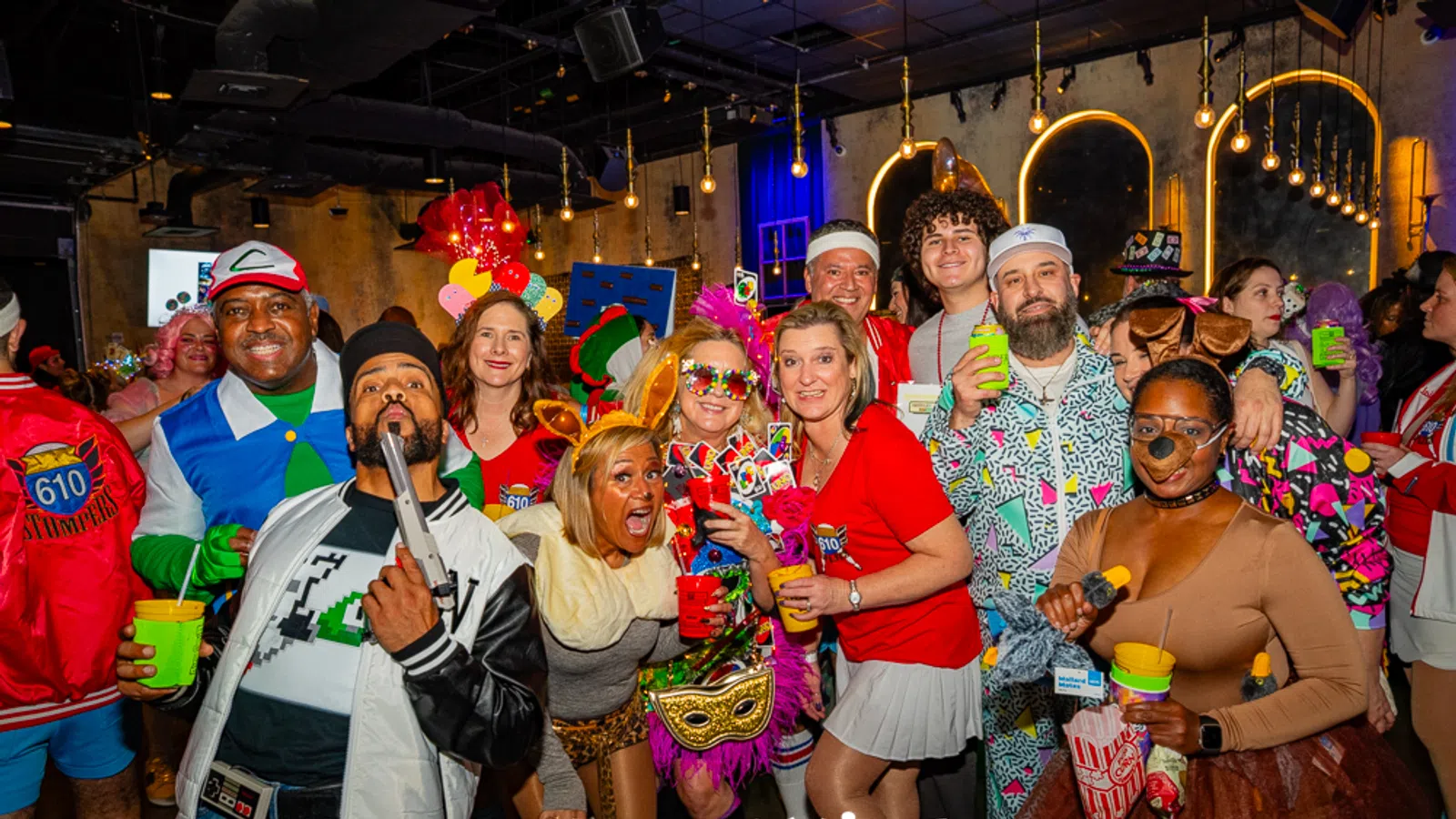 Group of people in colorful costumes enjoying a lively indoor party with themed decorations and drinks.