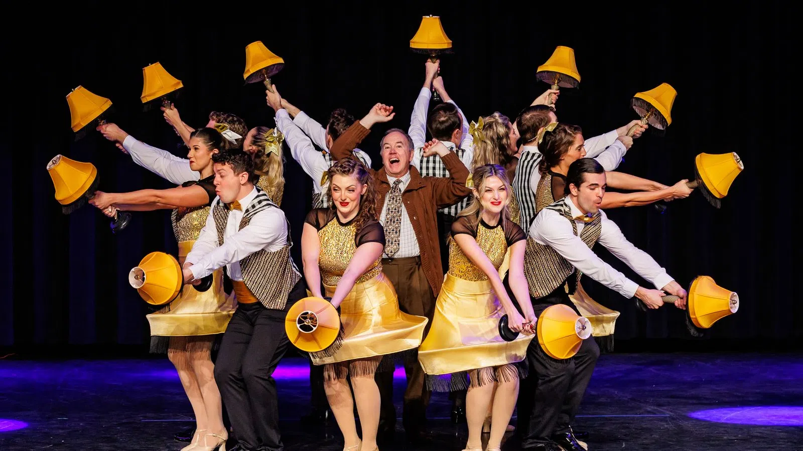 Performers in gold costumes dancing with yellow bell lamps on stage during a theatrical musical number