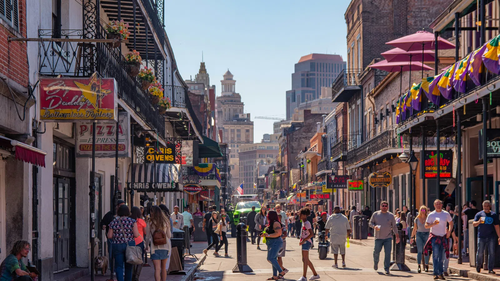 Busy urban street with pedestrians, restaurants, colorful banners, and historic buildings under clear sky.