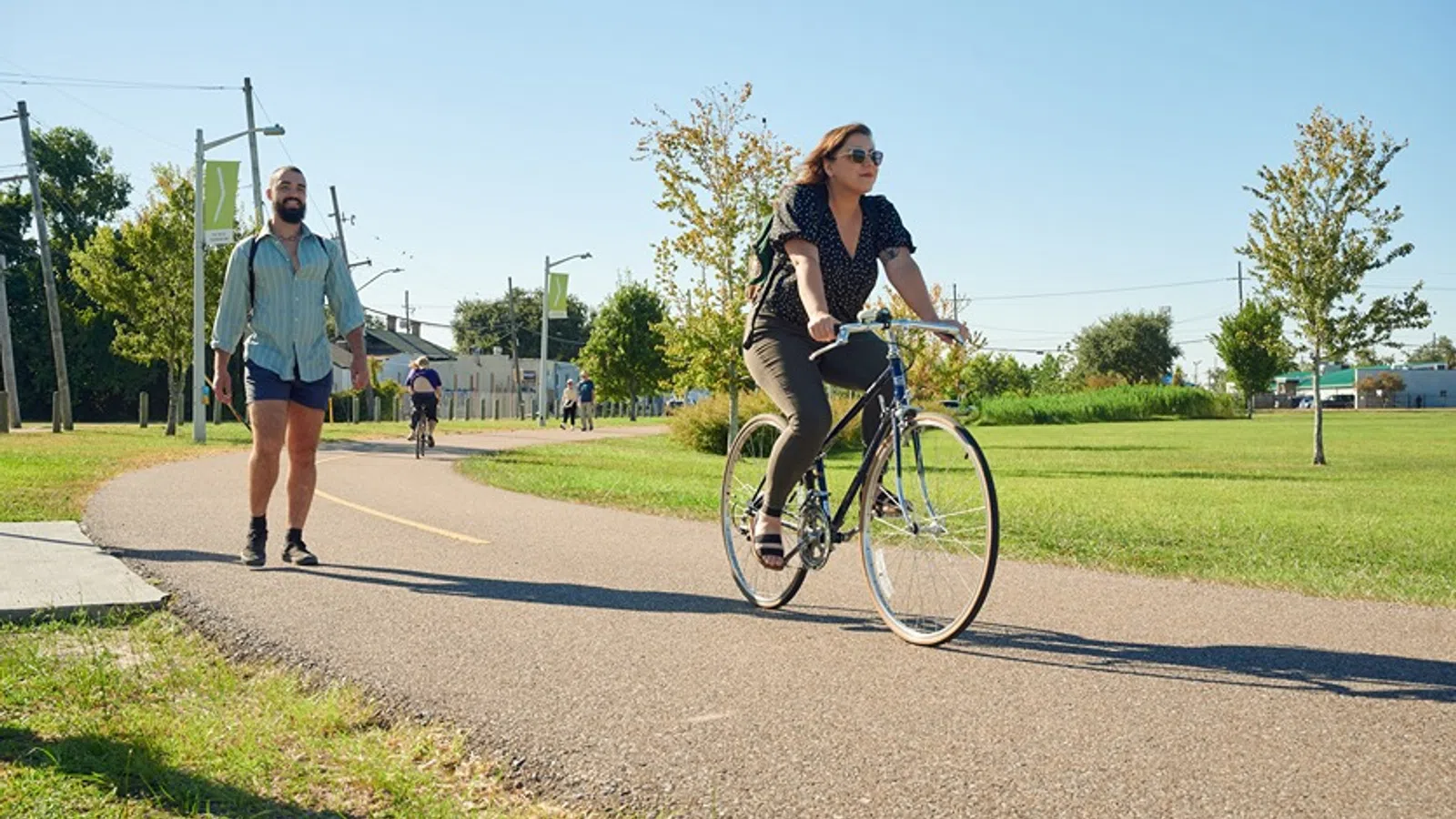 a woman riding a bicycle on a road with a man walking behind her