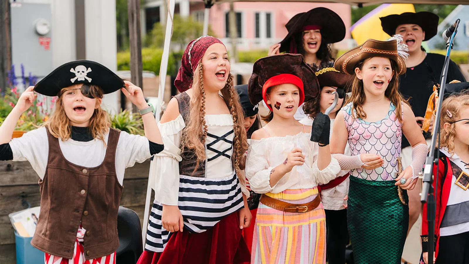 Group of children dressed as pirates and a mermaid performing outdoors with joyful expressions
