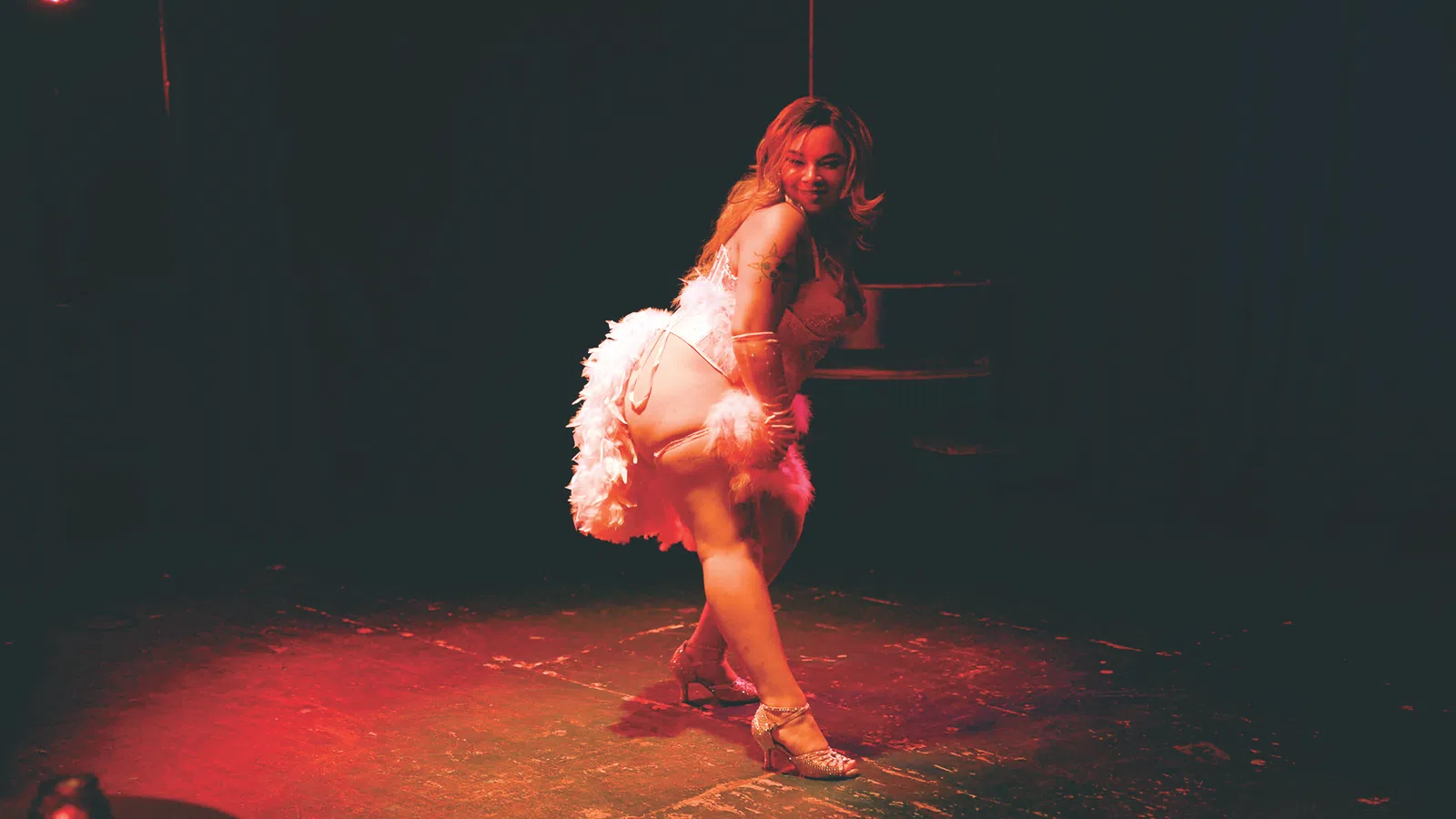 Woman in white feathered costume performing a dance on stage lit with red spotlight.
