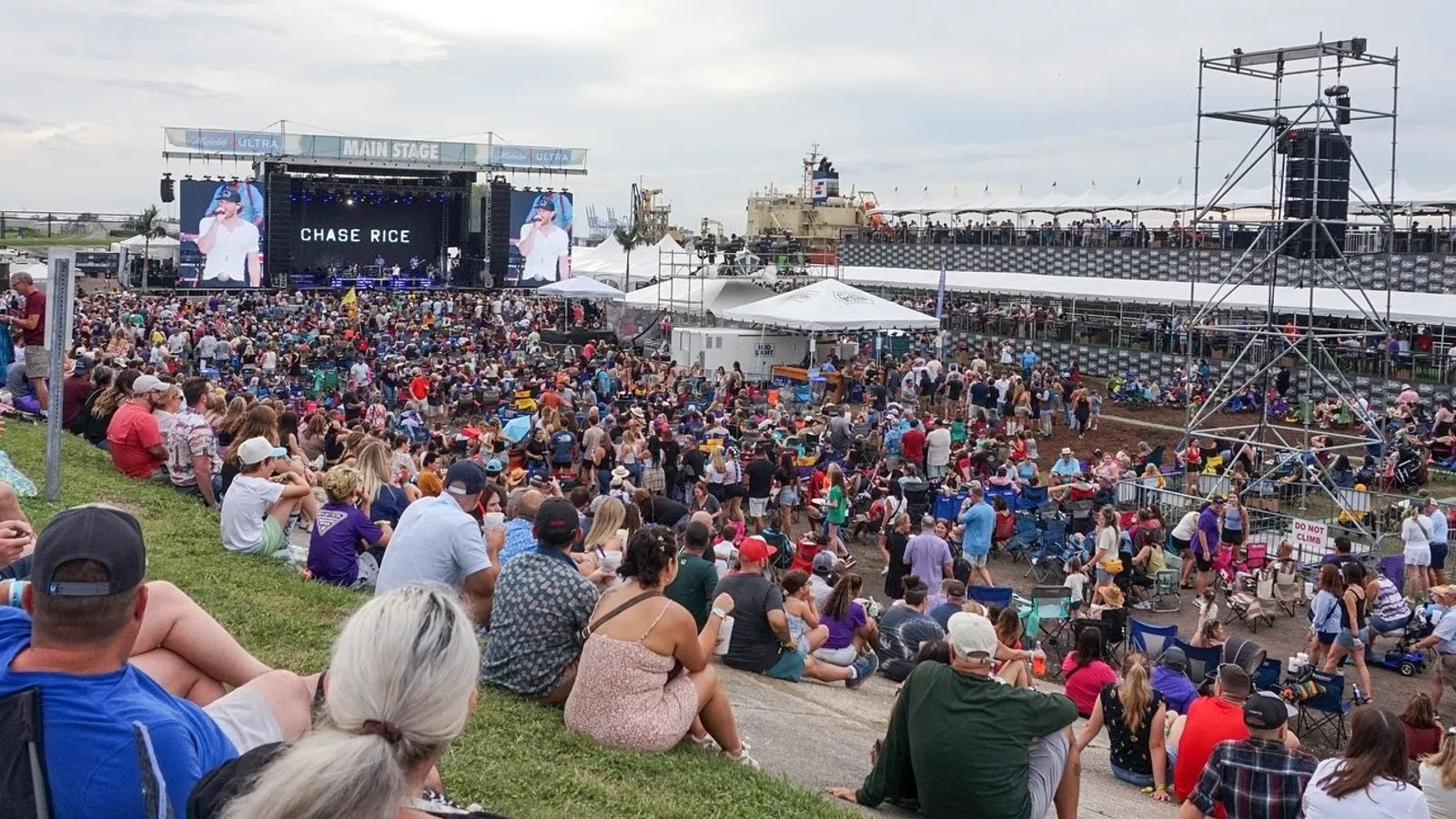 Large crowd enjoying an outdoor concert at the main stage with Chase Rice performing under a cloudy sky.
