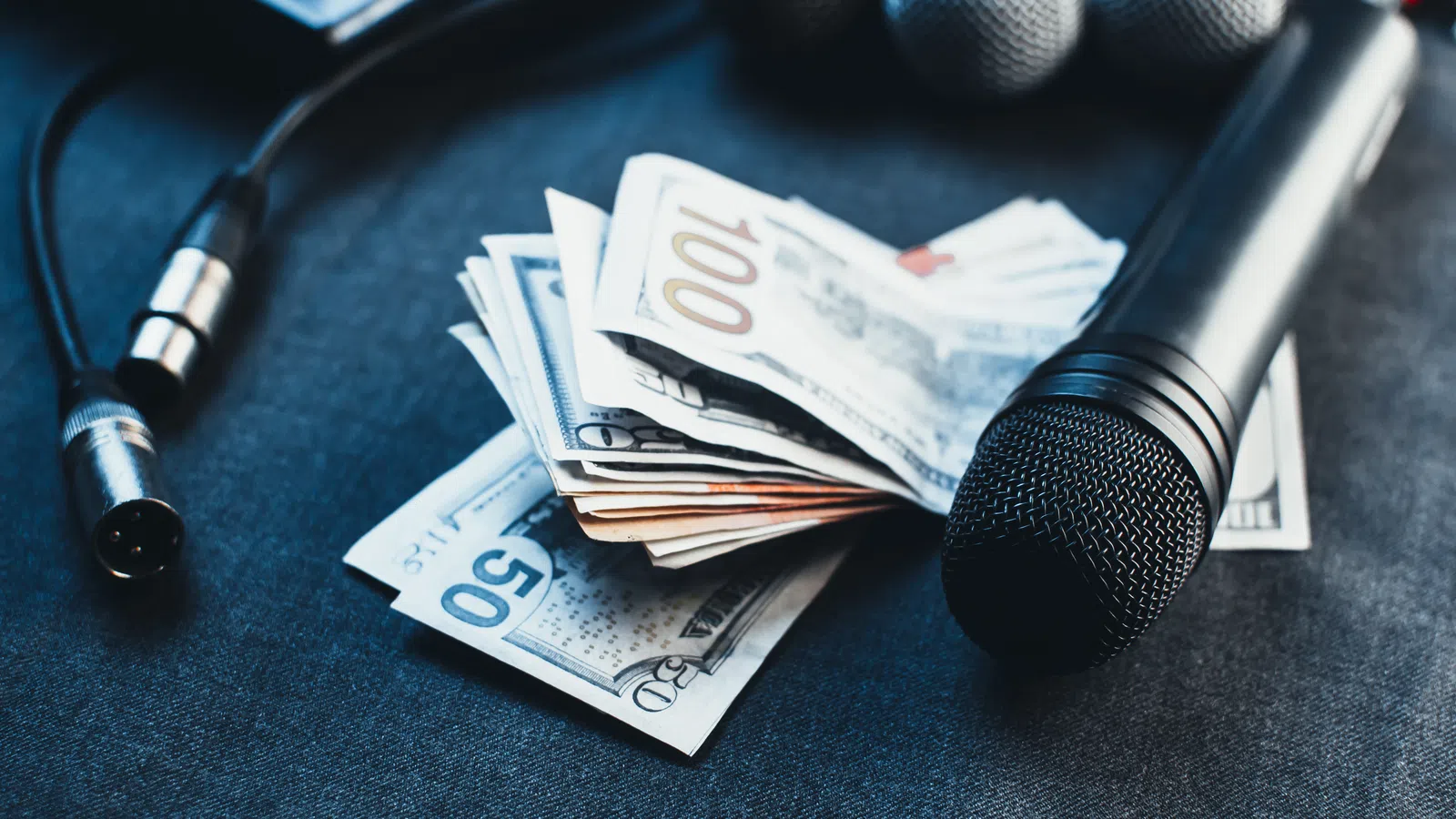 Microphones and audio cables placed next to a stack of US dollar bills on a dark surface