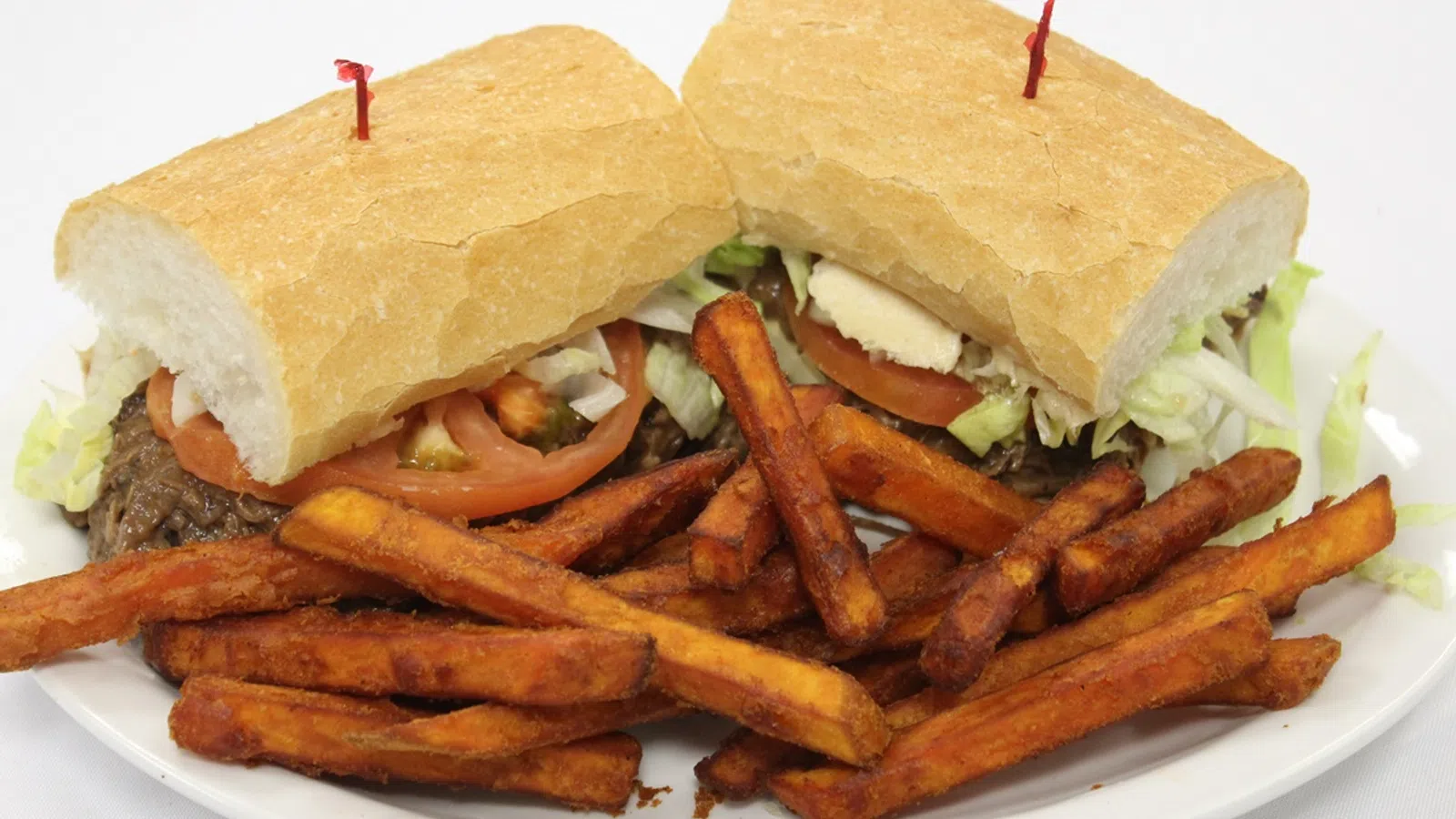 Sandwich with lettuce, tomato, and meat served with a side of crispy sweet potato fries on a white plate.