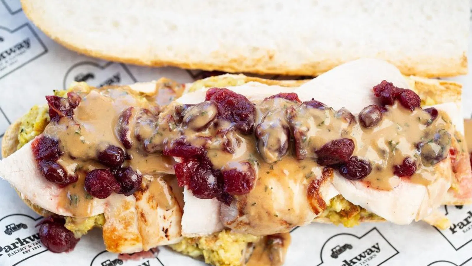 Turkey sandwich topped with gravy and cranberry sauce on a fresh baguette with stuffing inside.