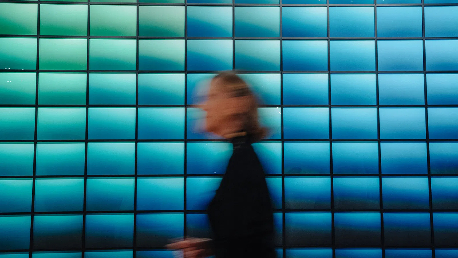 Blurred person walking in front of a vibrant blue tiled wall with gradient lighting