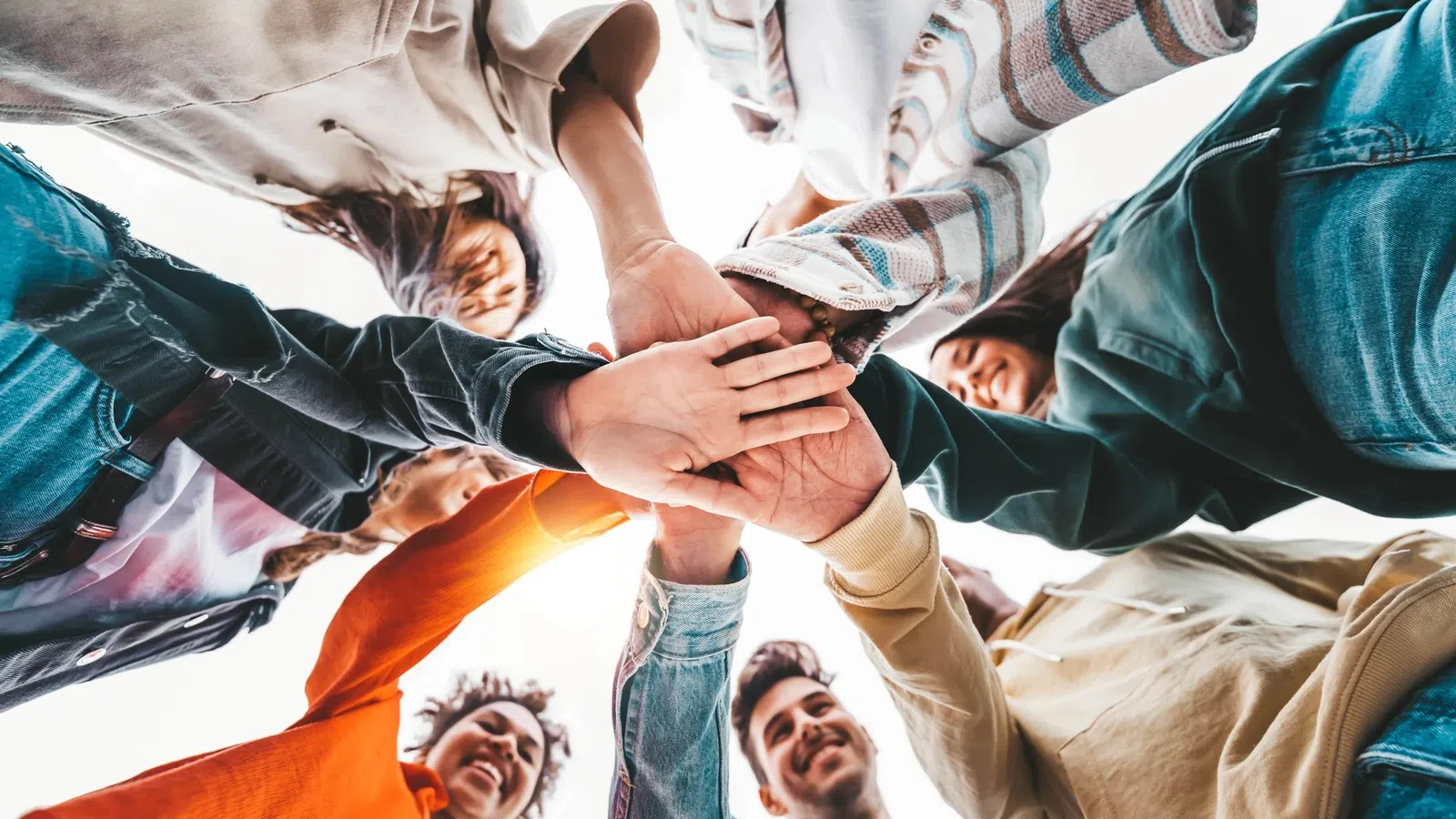 Group of diverse young people standing in a circle with hands joined together in unity and teamwork.
