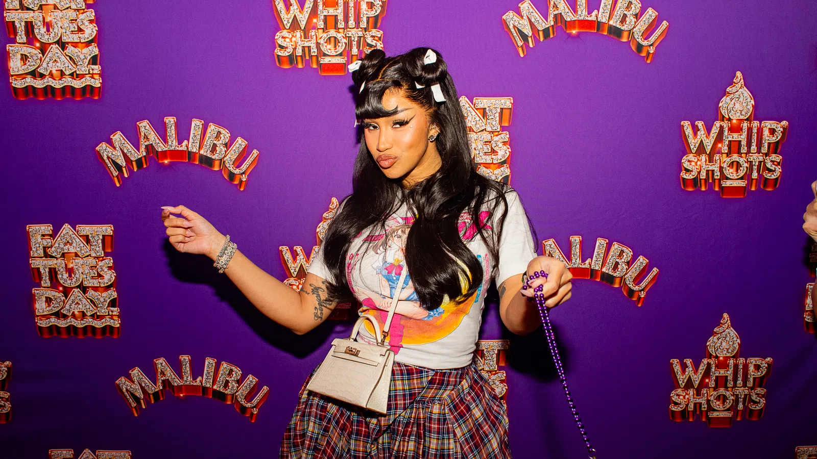 Woman with styled hair and plaid skirt poses in front of purple backdrop with Malibu and Whip Shots logos.