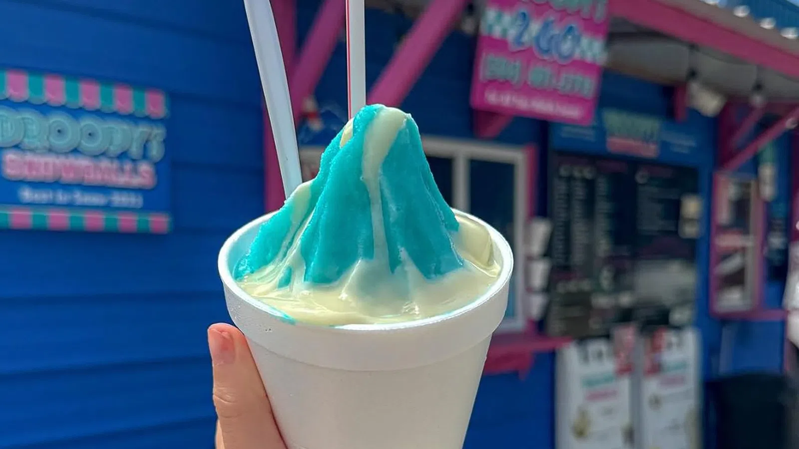 a hand holding a cup of ice cream with a straw