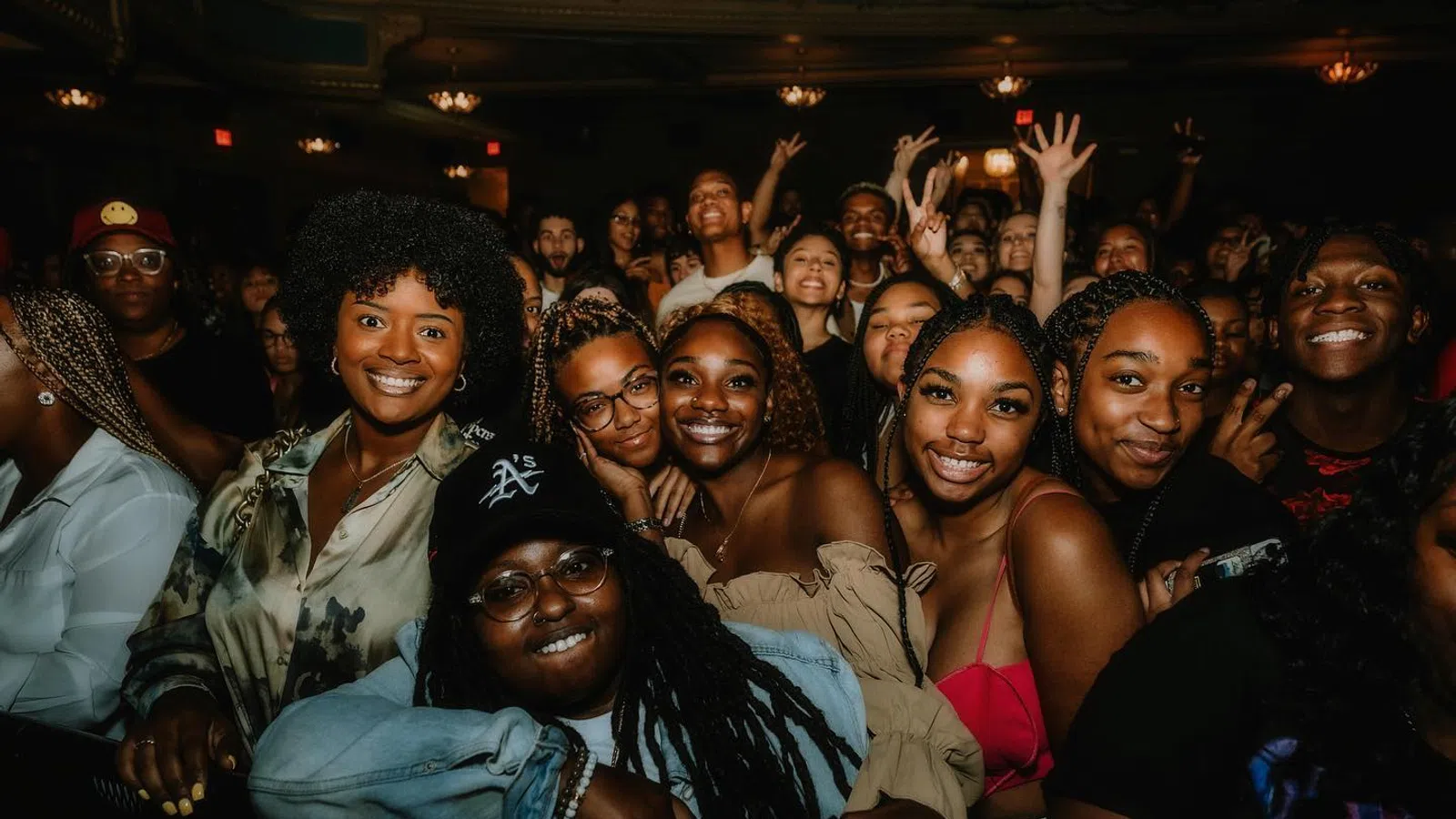 Group of diverse friends smiling and posing closely together at a lively indoor event with warm lighting.