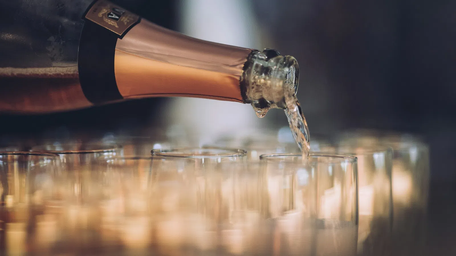 Champagne being poured from a bottle into a row of clear glasses at a celebration or event.