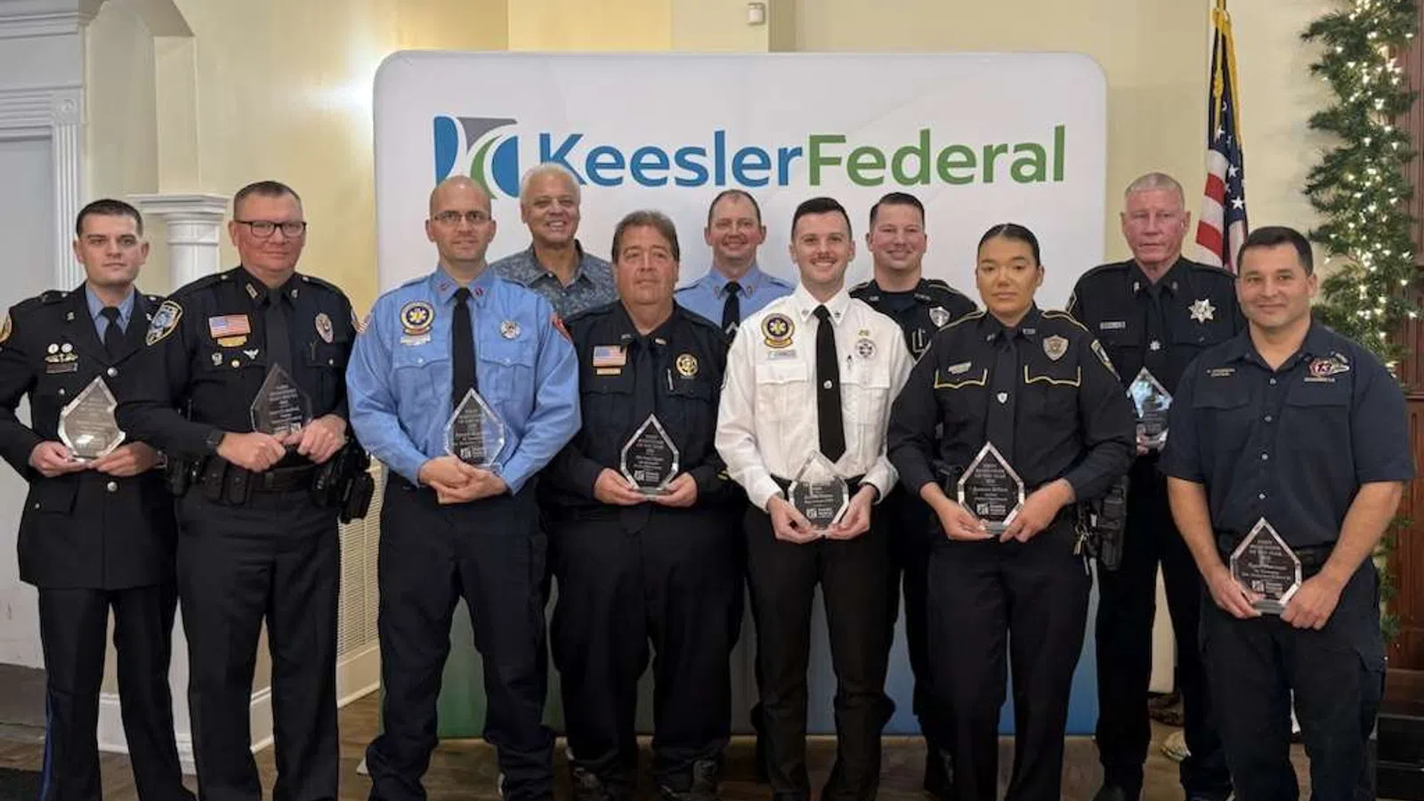 Group of uniformed police and emergency personnel holding awards in front of Keesler Federal backdrop indoors.