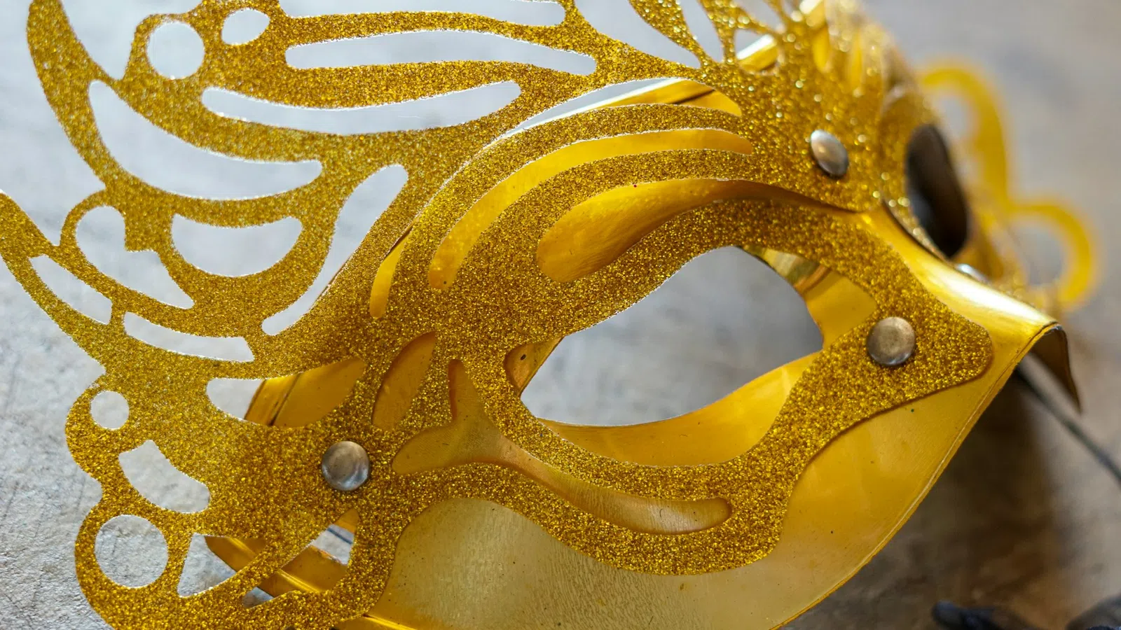 Close-up of an ornate golden masquerade ball mask with glitter and intricate cut-out patterns.