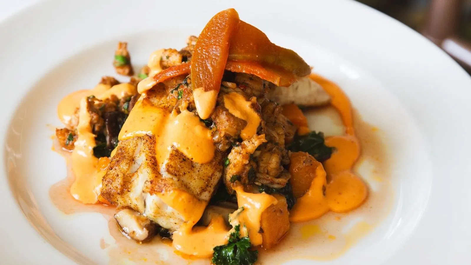 A beautifully plated dish with grilled fish, vegetables, and a rich sauce garnished with a slice of orange.