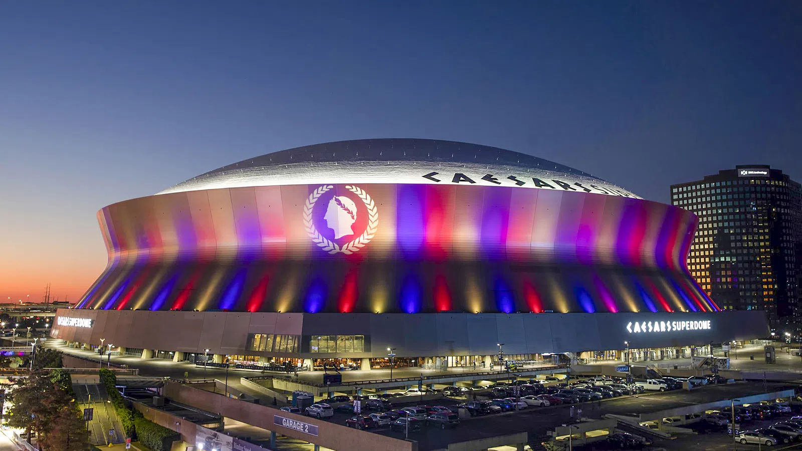 Caesars Superdome lit up with red, blue, and yellow lights at dusk in New Orleans, Louisiana.