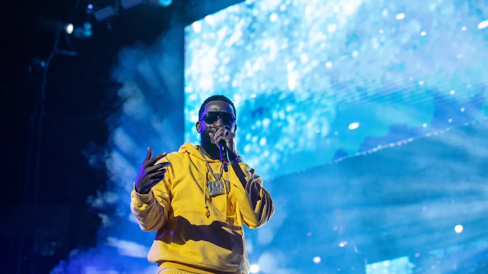 a man wearing a yellow jacket and sunglasses with his hand up