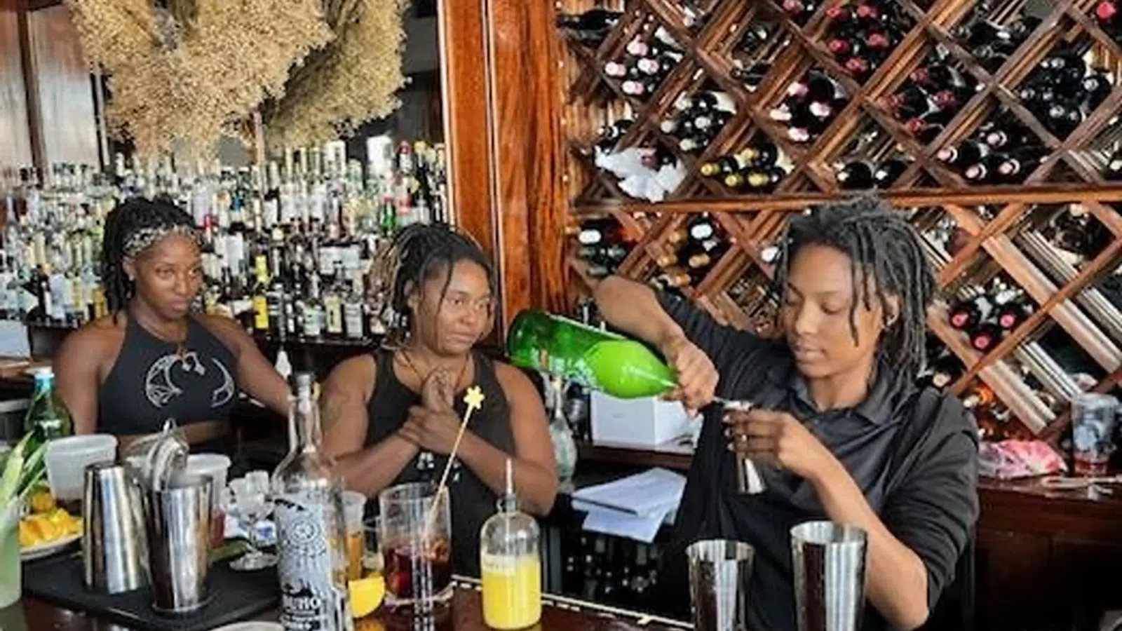 a group of women sitting at a bar drinking from a green bottle