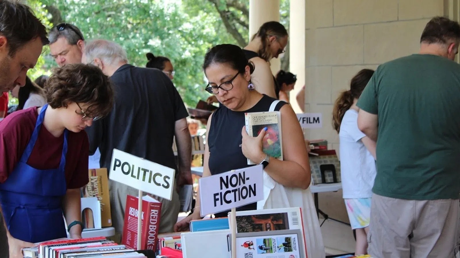 People browsing books at an outdoor book fair with nonfiction and politics sections visible.