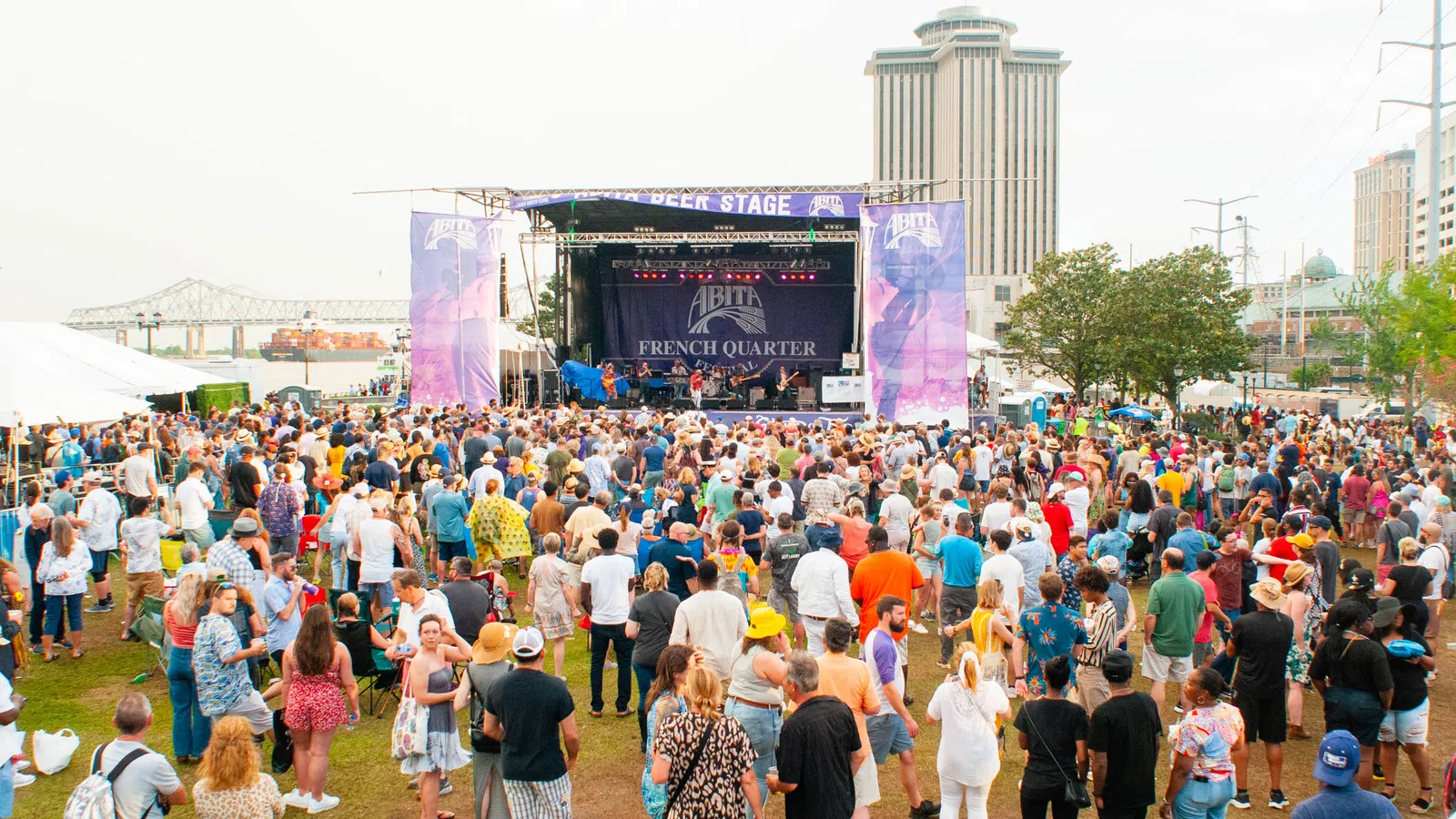 Large crowd enjoying live music at an outdoor festival near a waterfront stage and city skyline.