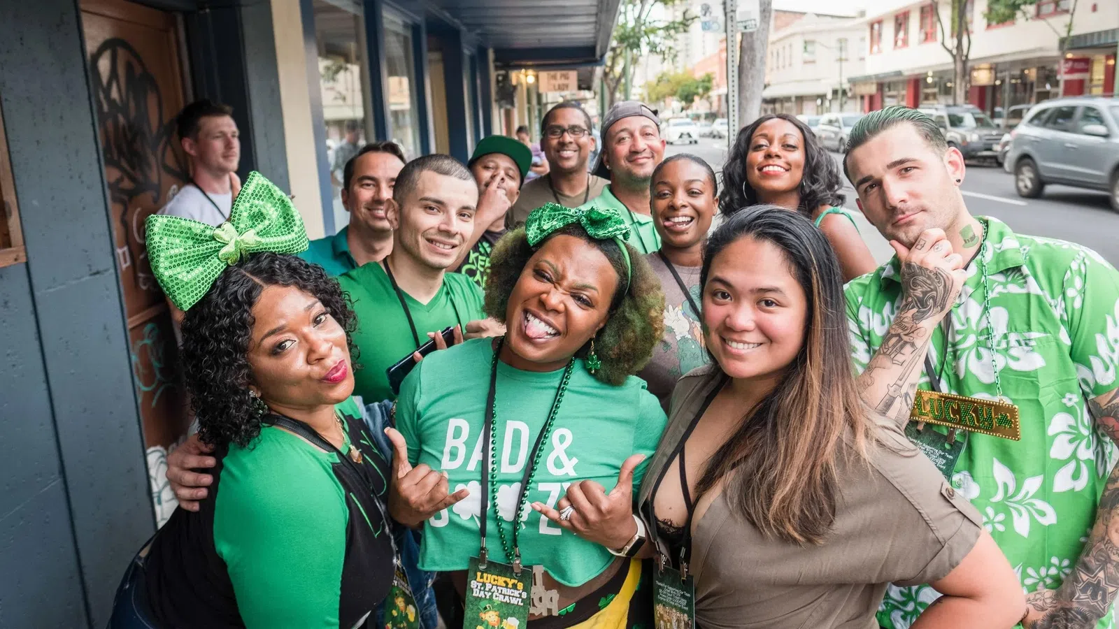 Group of diverse people dressed in green celebrating and smiling outdoors on a city street party.