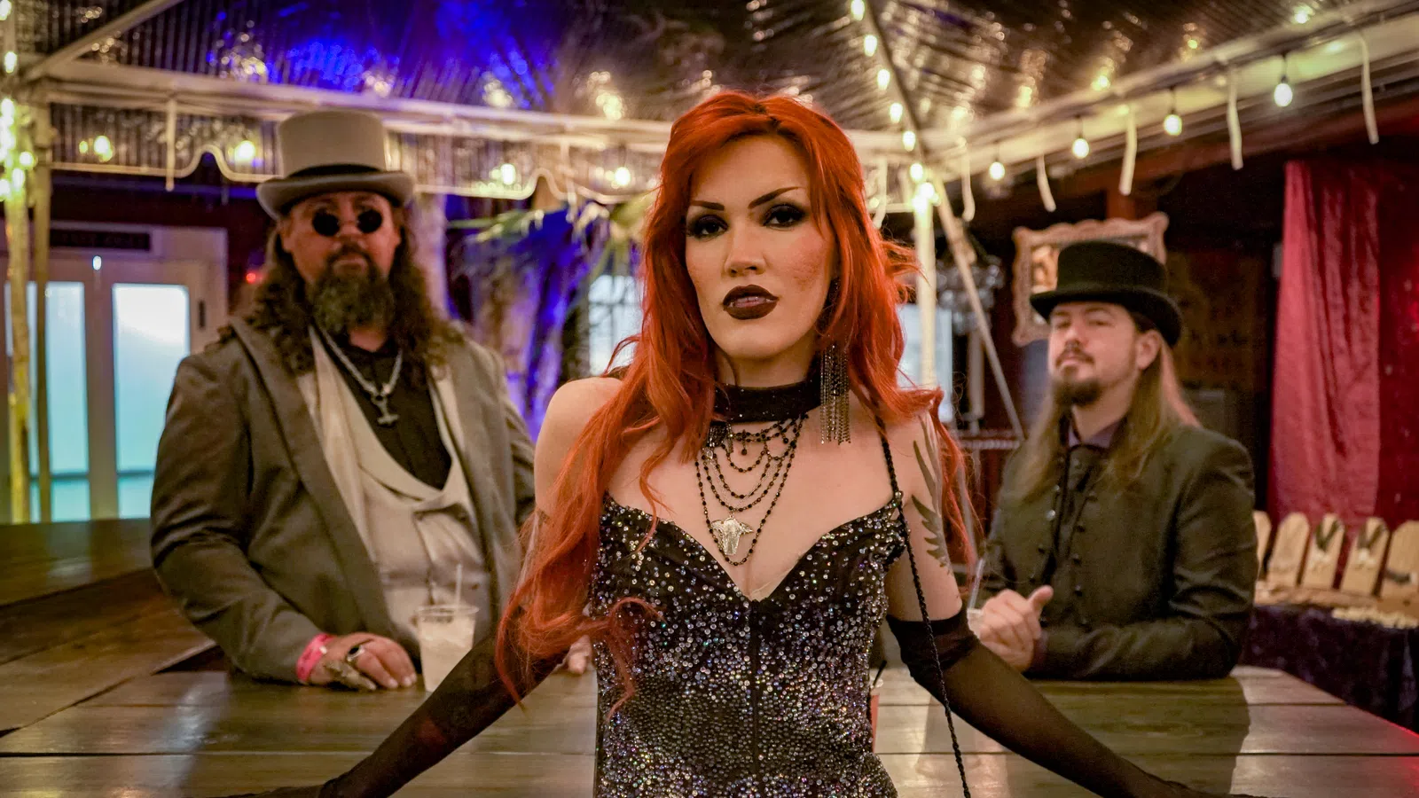 Three people in gothic steampunk attire posing indoors with dramatic lighting and dark vintage decor.