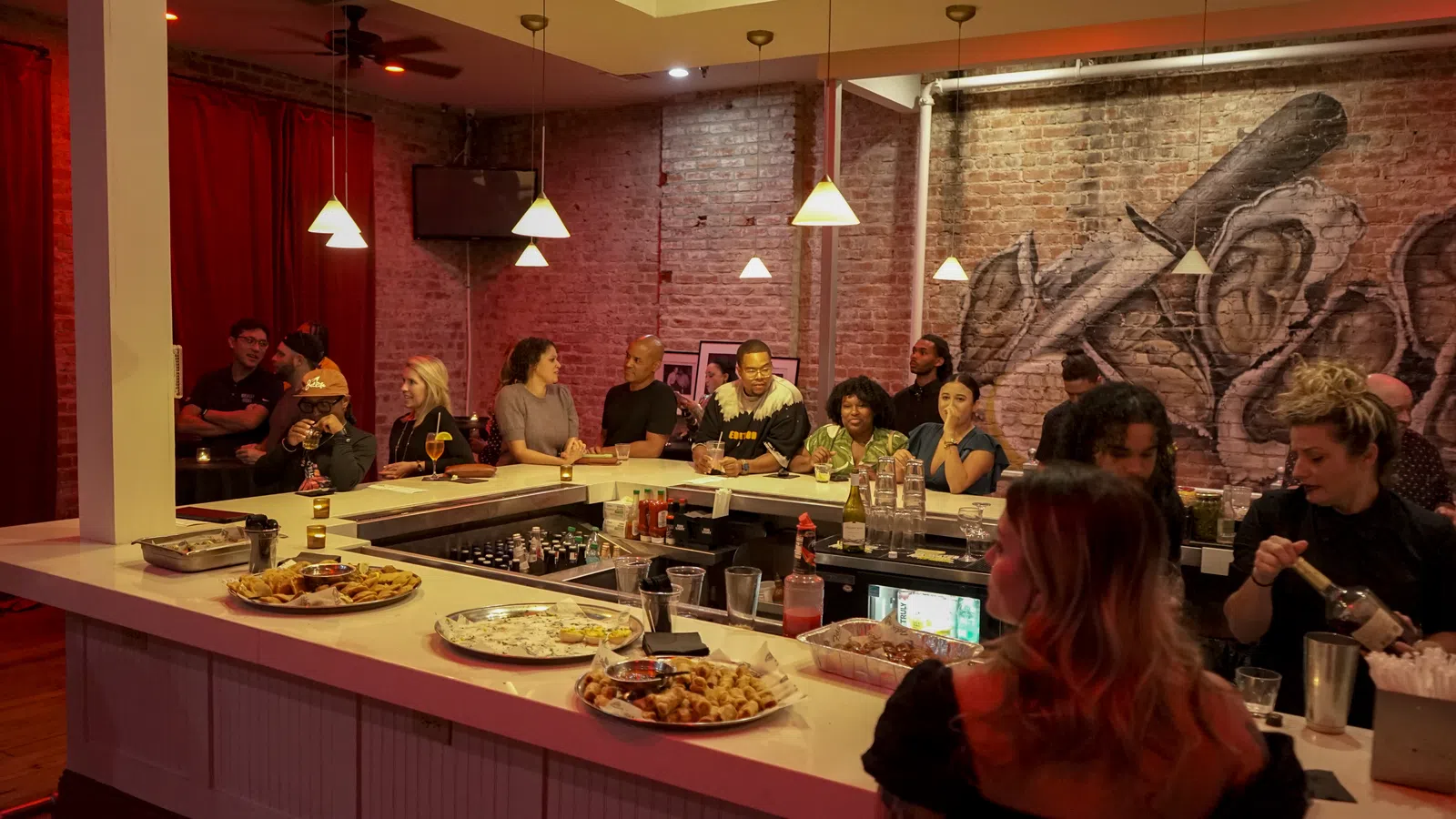 People socializing and enjoying drinks around a modern bar with exposed brick walls and warm pendant lighting.