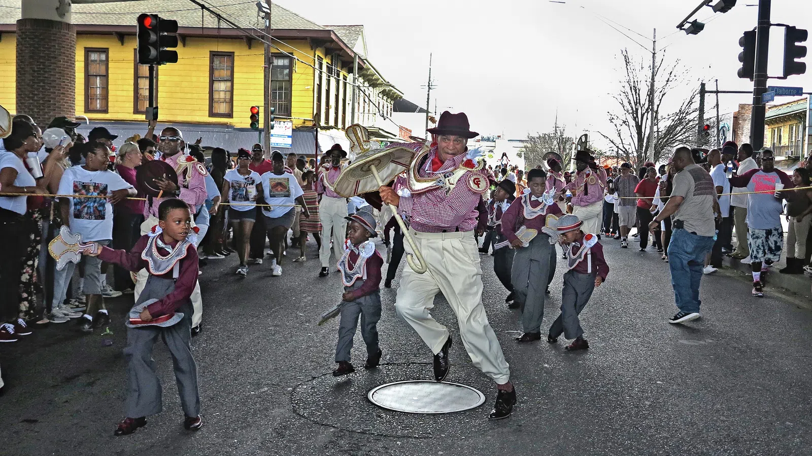 Children and adult dancers in traditional costumes perform on a street during a lively parade with onlookers.