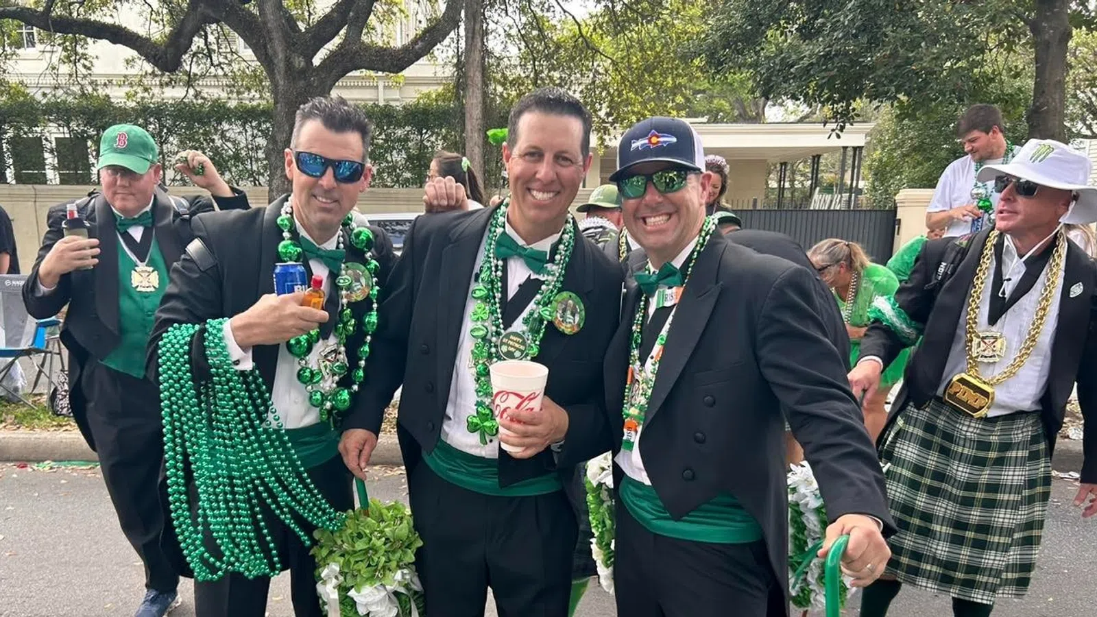 Group of men in formal wear with green accessories celebrating outdoors during a festive parade or event.
