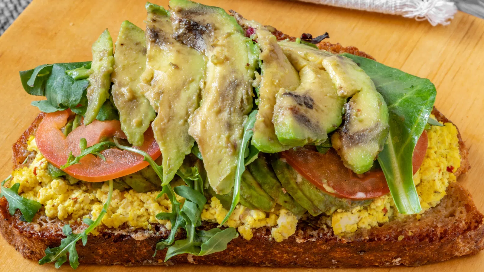 Delicious open-faced sandwich with avocado, tofu, tomatoes, and greens on rustic bread.