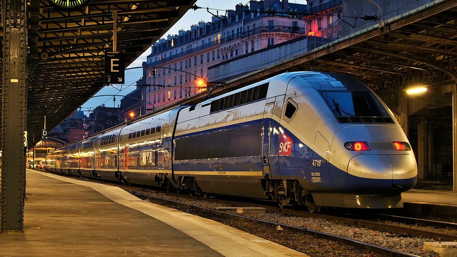 High-speed TGV train at a Paris station platform during twilight with city buildings in background