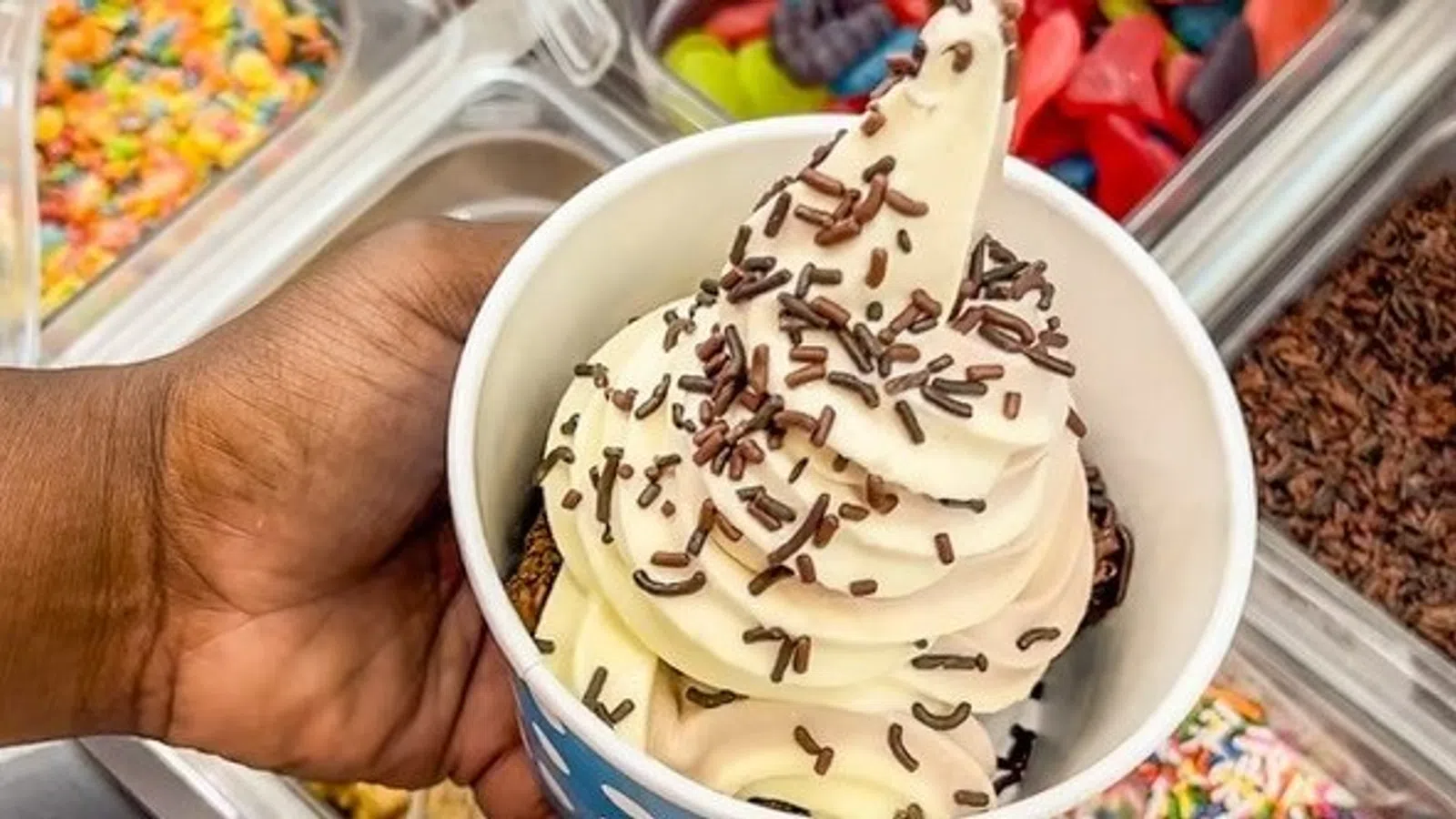 a hand holding a cup of ice cream in a plastic container with candy