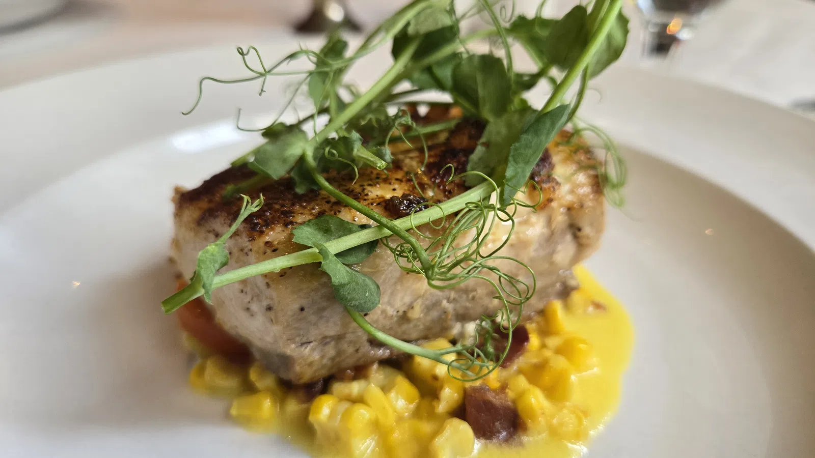 Grilled fish fillet topped with fresh pea shoots served on creamy corn sauce with bits of bacon.