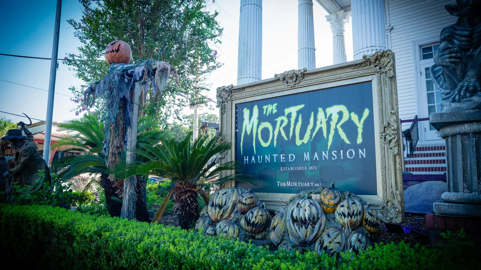 Sign for The Mortuary Haunted Mansion surrounded by Halloween pumpkins and spooky decorations outside a white columned building.