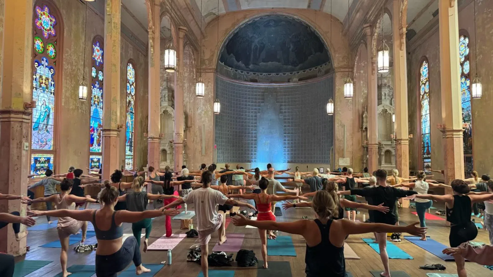 Group yoga session in a historic church with stained glass windows and wooden floors.