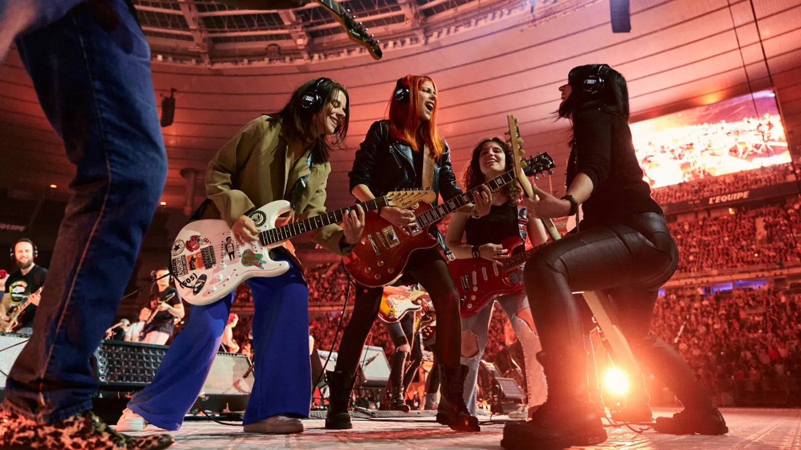 Energetic band performing live on stage with guitars and vibrant crowd in a large stadium concert.