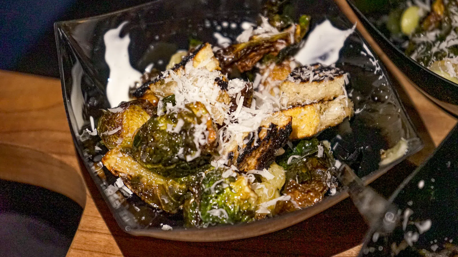 Roasted Brussels sprouts topped with grated cheese served in a black bowl on a wooden table