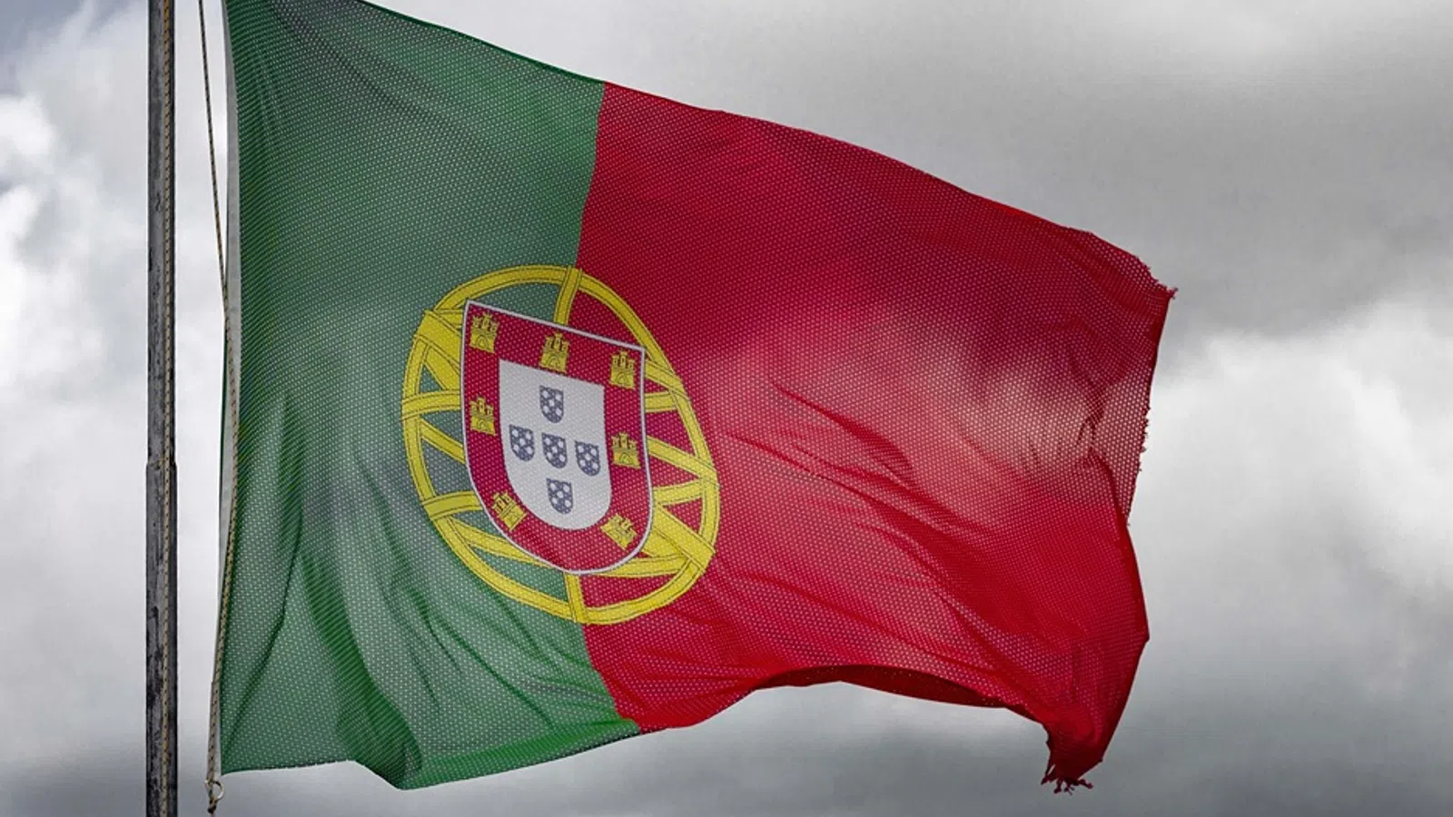 Portuguese national flag waving on a pole against a cloudy sky background