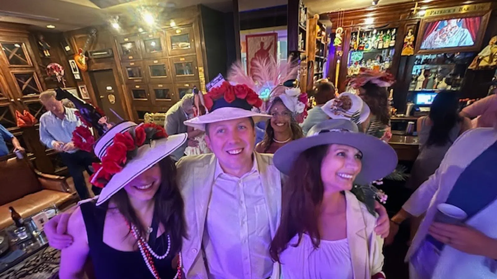 Group of smiling people wearing colorful hats enjoying a lively indoor party with drinks and wooden decor.