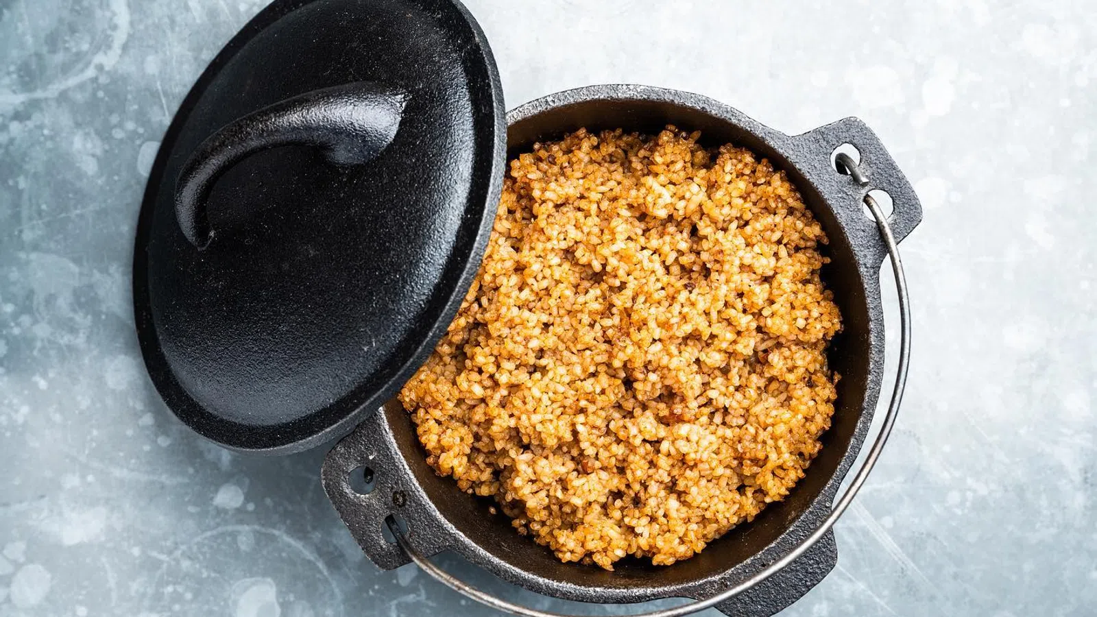 Cast iron pot with cooked seasoned bulgur wheat on a light textured surface with lid ajar