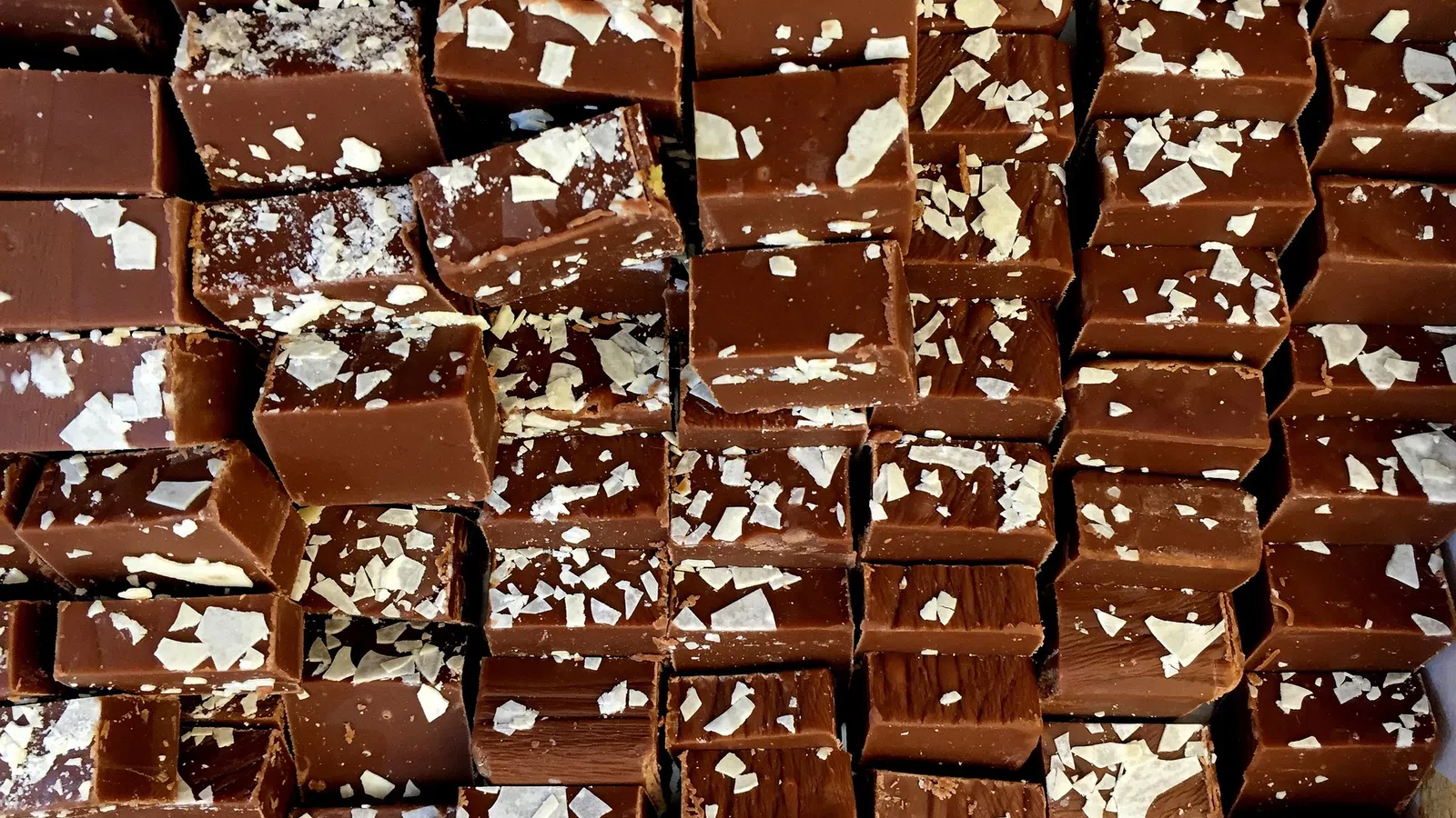 Close-up of bite-sized chocolate cubes topped with white flakes arranged in rows.